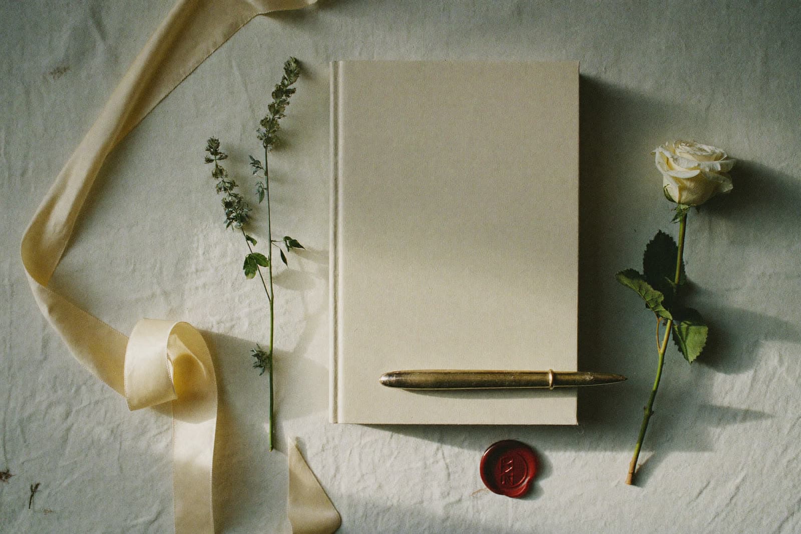 A linen-bound planning journal styled with silk ribbon, a brass pen and a white rose